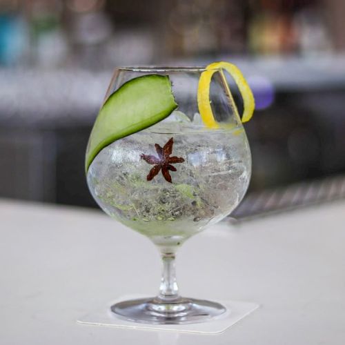 A delicate cocktail with a lime wheel garnish, mint sprig, and a tiny parasol, served in a short glass on a reflective surface.