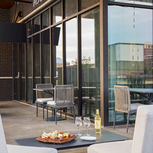 A modern outdoor cafe with glass walls, potted plants, and sleek seating by a street, sunlight streaming in and a cozy urban vibe.