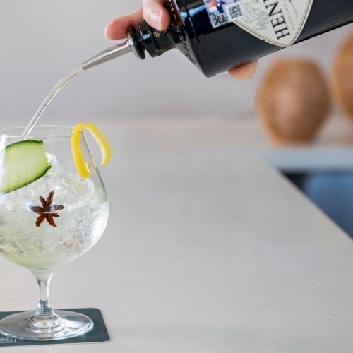 A hand is about to place a wooden ball into a clear glass bowl with a yellow flower inside, on a white surface.