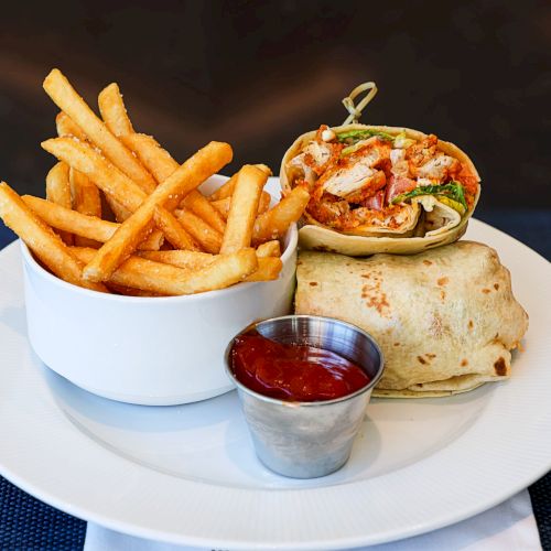 A dessert plate with thin waffle fries stacked like fries, topped with ice cream, fruits, and a drizzle of sauce on a blue plate.