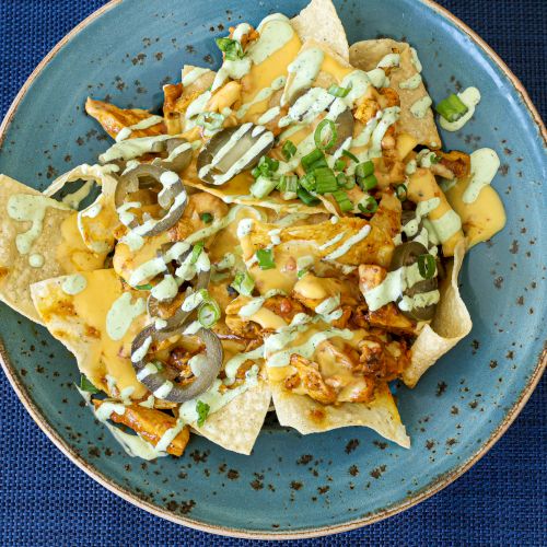 A plate of nachos topped with melted cheese, chopped vegetables, and salsa on a blue plate.