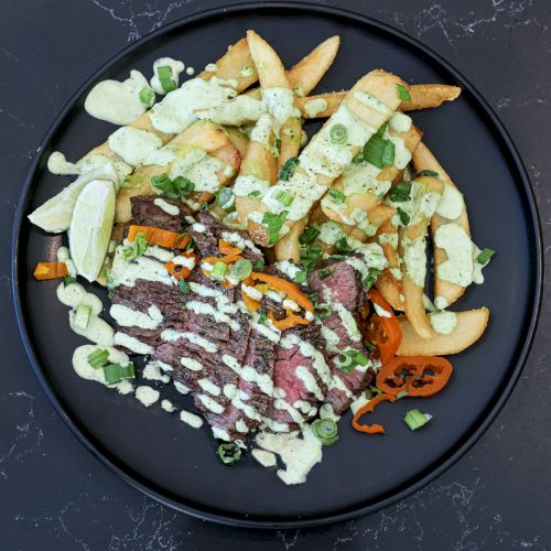 A plate of fries topped with drizzle and creamy sauce, garnished with herbs and a side of dipping sauce.