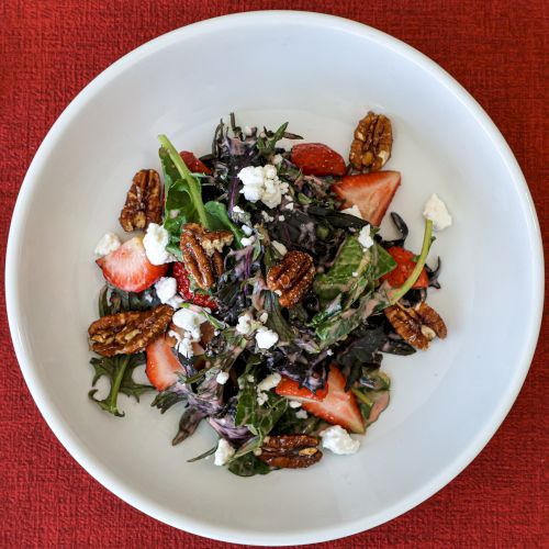A colorful salad or grain bowl featuring greens, seeds, and shredded toppings on a white plate, with a mix of vibrant veggies and possibly quinoa.