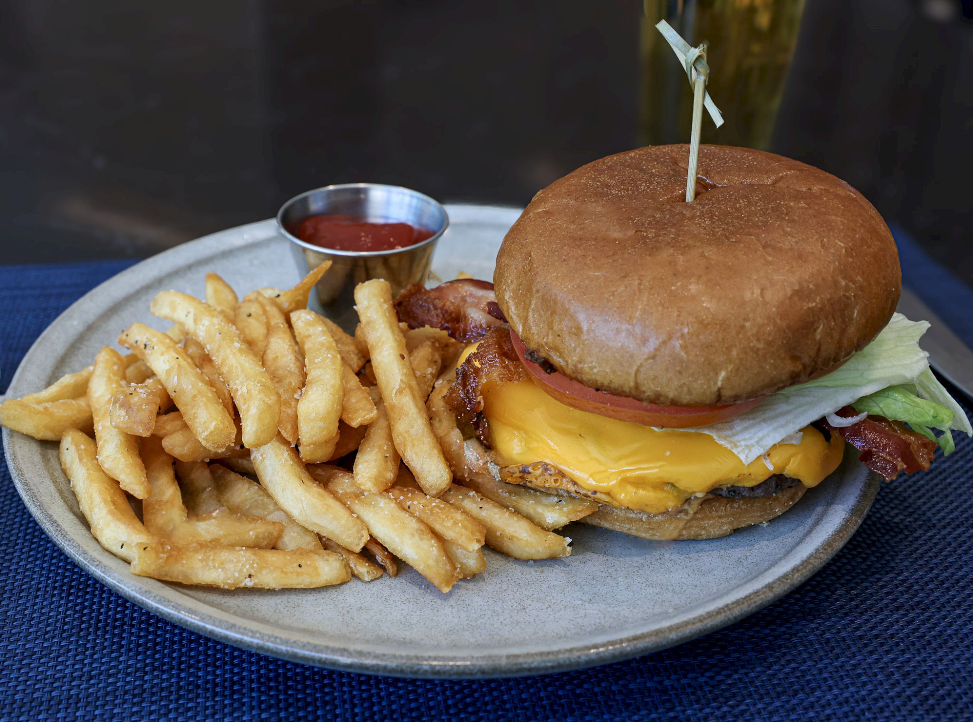 A classic cheeseburger with lettuce, cheese, and bacon on a bun, served with a generous side of French fries and dipping sauce on a plate.