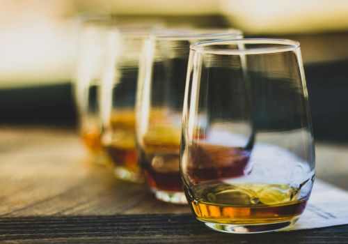Three glasses of whiskey on a wooden table, out-of-focus background, warm tones, casual drink setting.