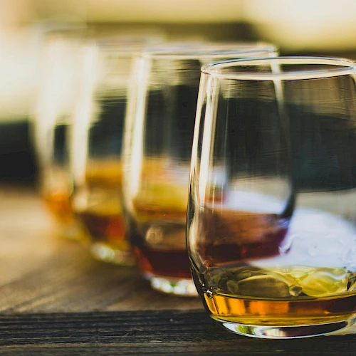 Three glasses of whiskey on a wooden table, out-of-focus background, warm tones, casual drink setting.