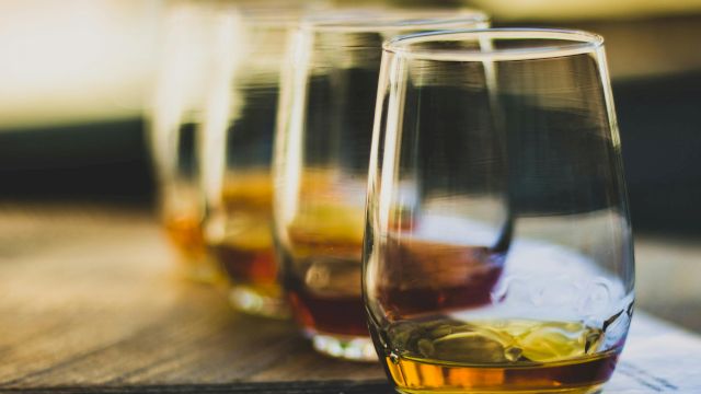 Three glasses of whiskey on a wooden table, out-of-focus background, warm tones, casual drink setting.